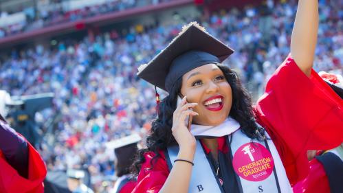 smiling student wearing cap and gown wearing a first generation sticker
